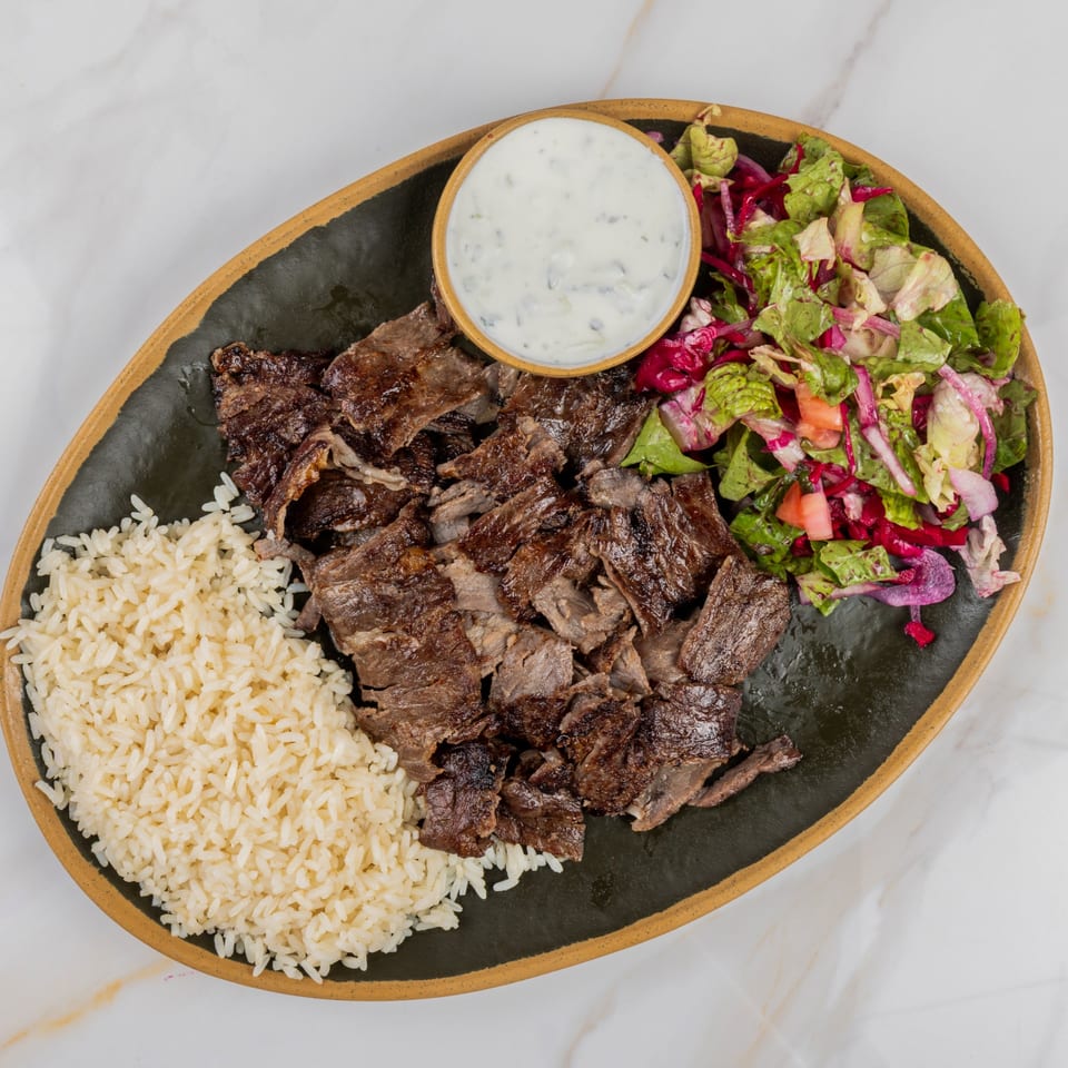 Marash Mediterranean doner kebab plate with sliced meat, rice, salad, and a side of white sauce.