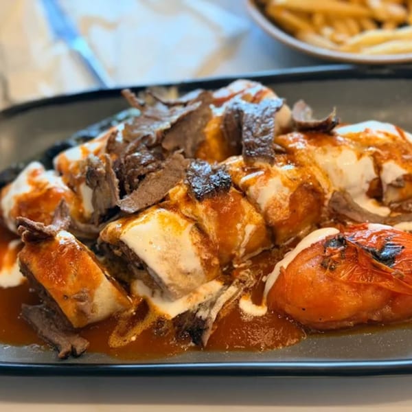 Marash Mediterranean's Iskender kebab, featuring sliced meat, tomato sauce, yogurt, and grilled tomatoes.