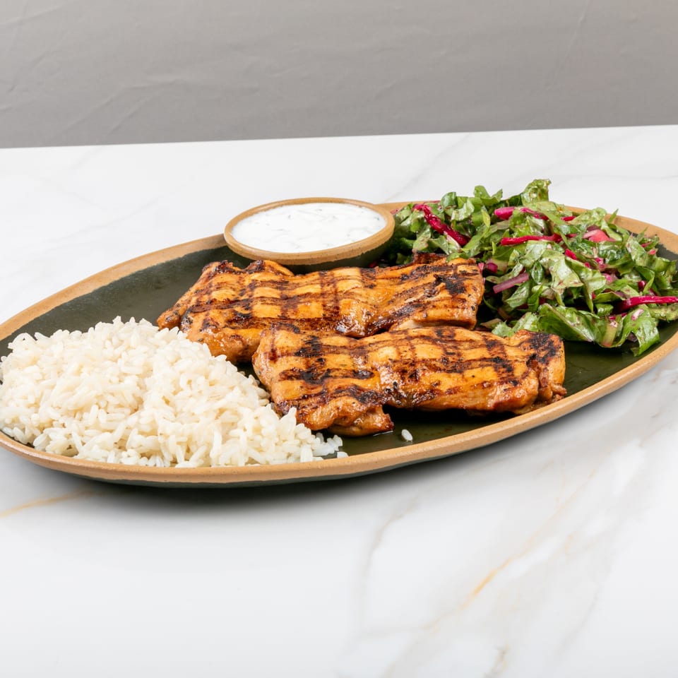 Marash Mediterranean grilled chicken with rice, salad, and a side of white sauce on a dark plate.
