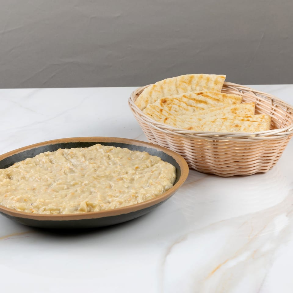 Marash Mediterranean baba ghanoush in a black bowl with a basket of pita bread.